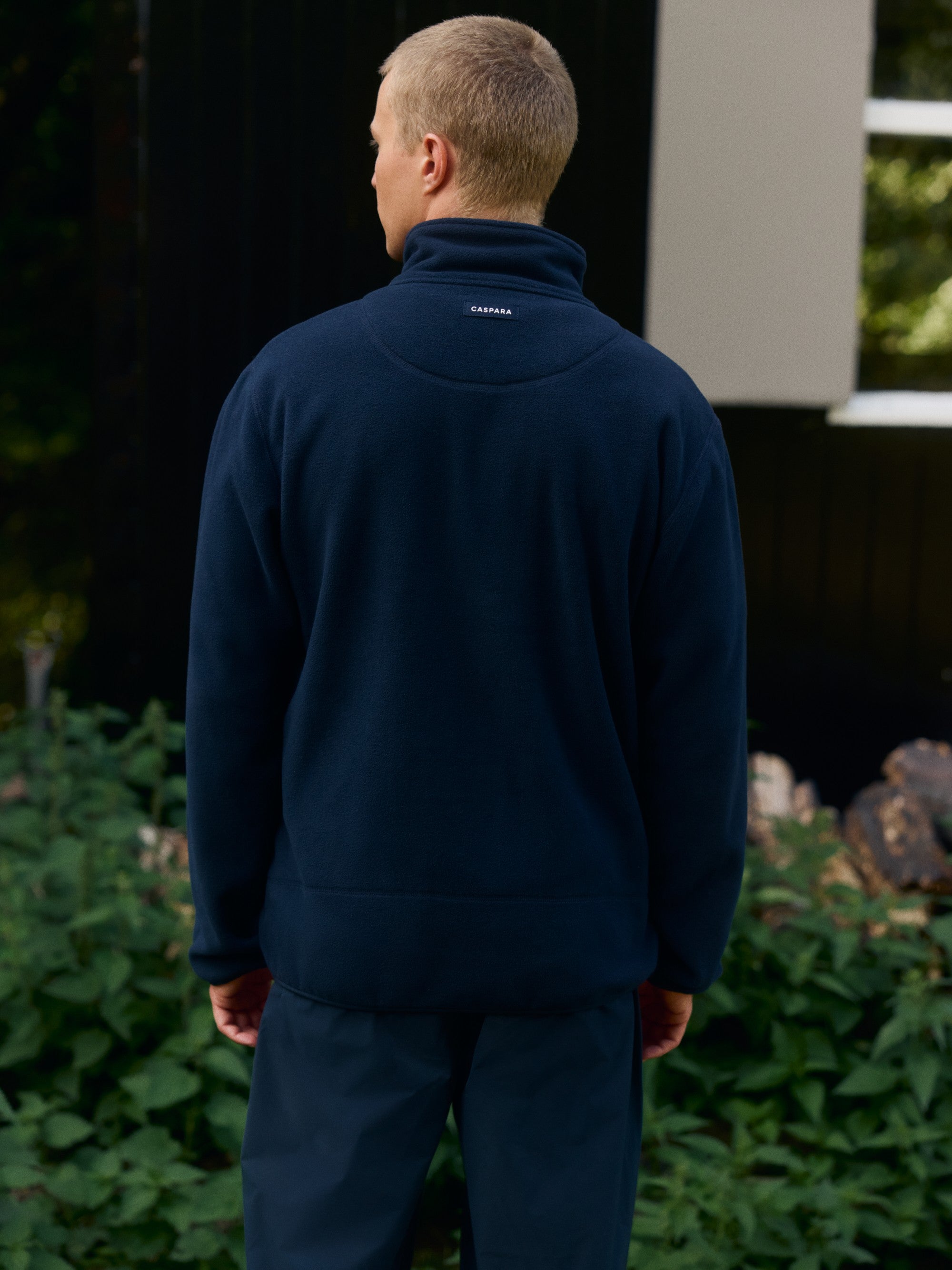 Back view of a man wearing a navy CASPARA polar fleece pullover outdoors.